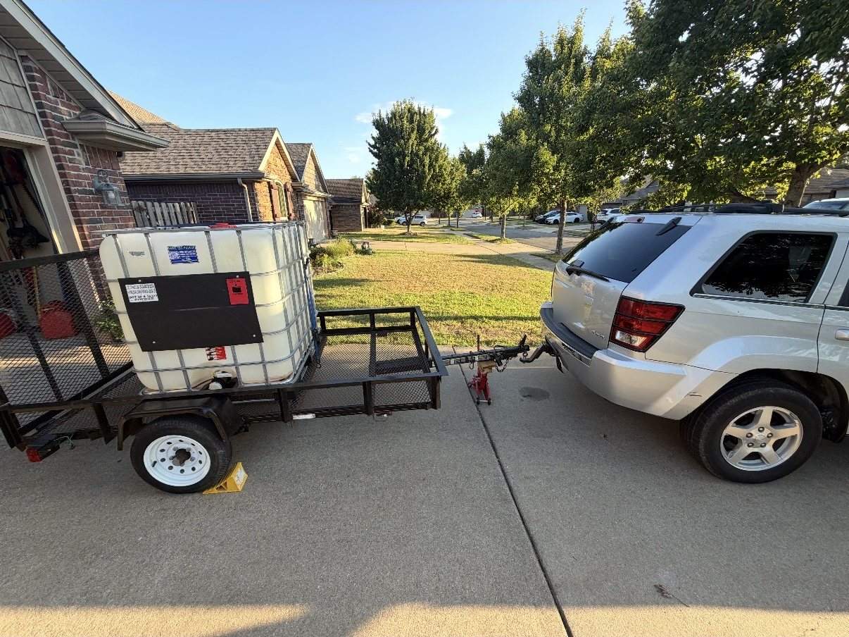 The Wash It Wash It trailer with its water tank, hitched and ready in a Fayetteville driveway